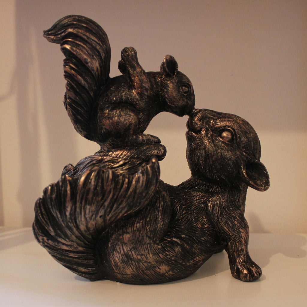 Bronze resin sculpture of a squirrel and pup on a white surface with a neutral background